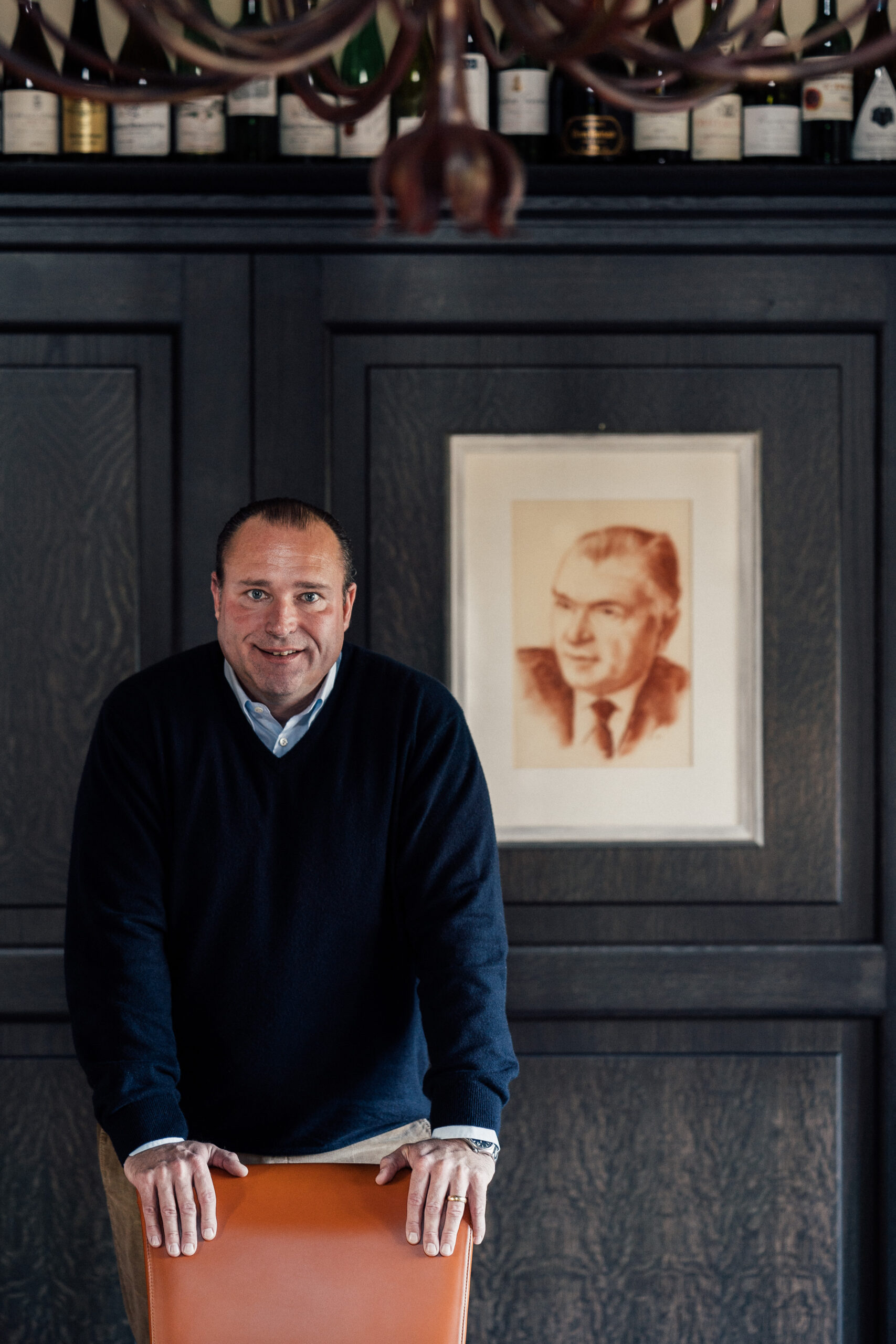 Nik Weis owner of a German winery, posing in front of a potrait of his grandfather. 