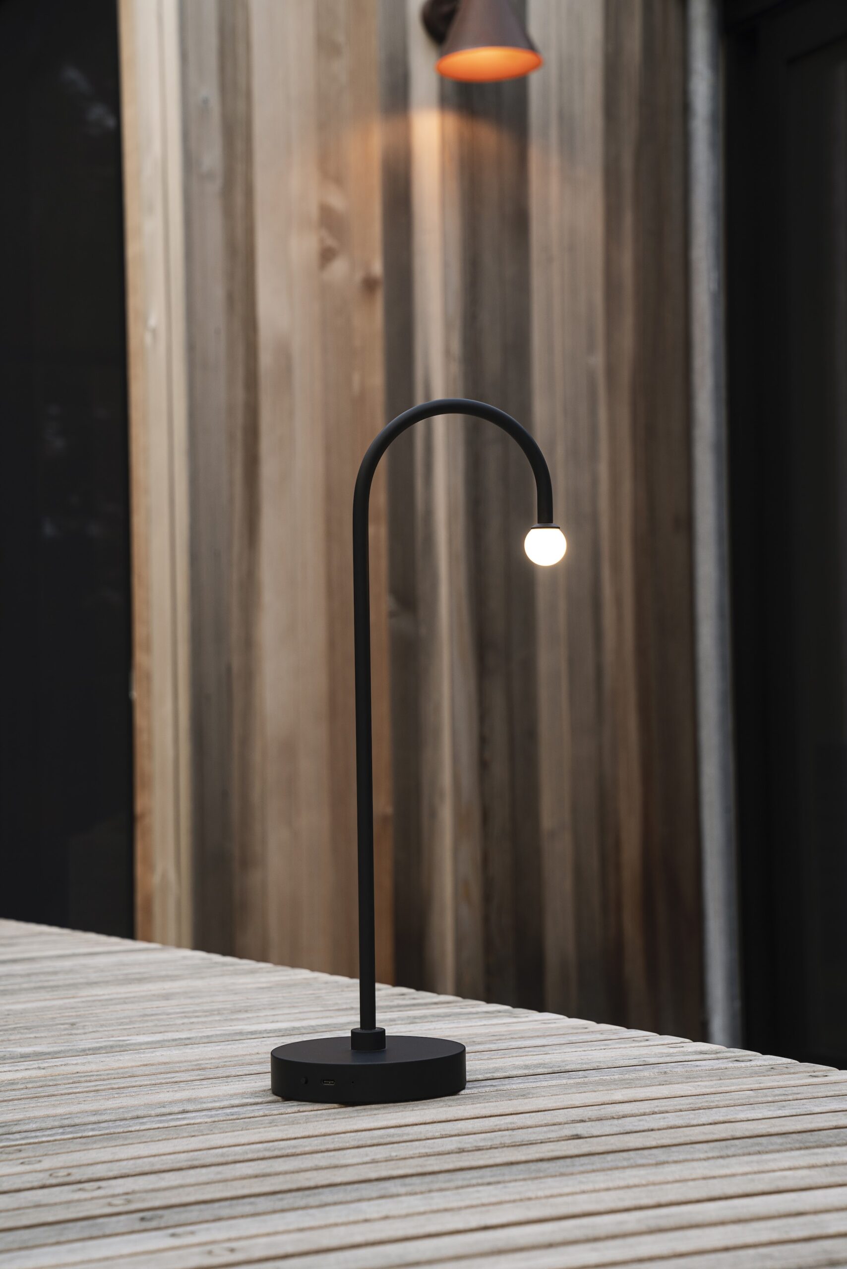 Thin black table lamp with small hanging bulb. Minimalist furniture.